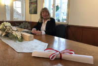 Standesbeamtin Dagmar Berger sitzt an einem Holztisch im Sitzungssaal des Rathauses. Auf dem Tisch steht ein Schutzfenster aus Plexiglas.